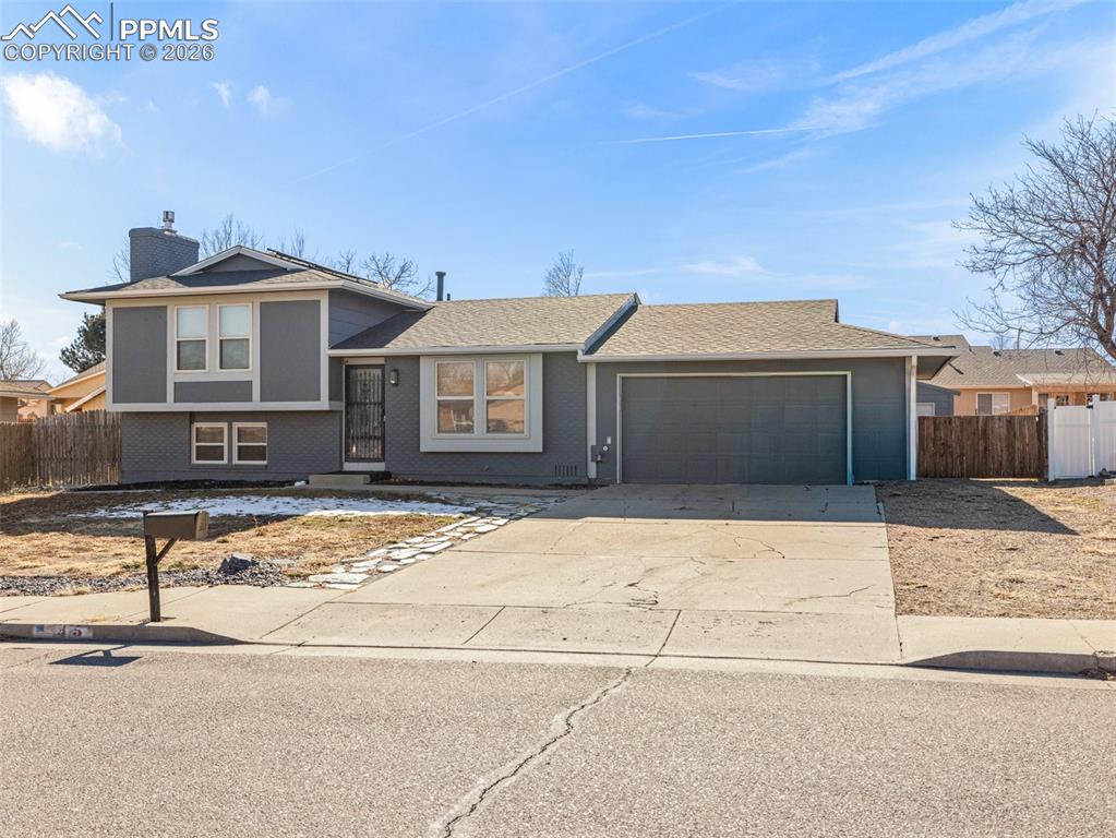 Caption: Tri-level home featuring driveway, a chimney, brick siding, roof with shingles, and an attached gara