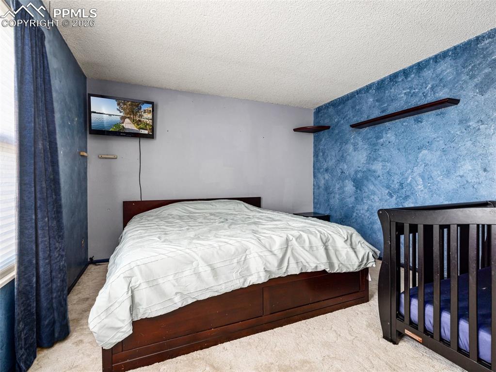 Image 16 of 30: Bedroom with carpet flooring, a textured ceiling, and an accent wall