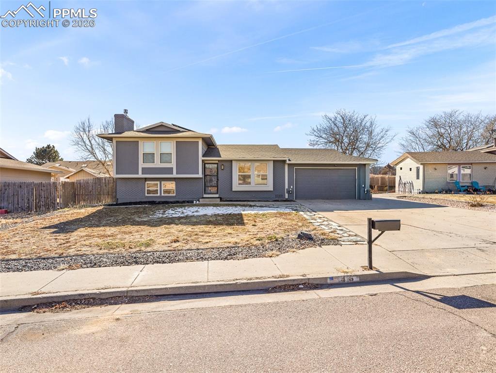 Image 2 of 30: Split level home with driveway, a chimney, and an attached garage