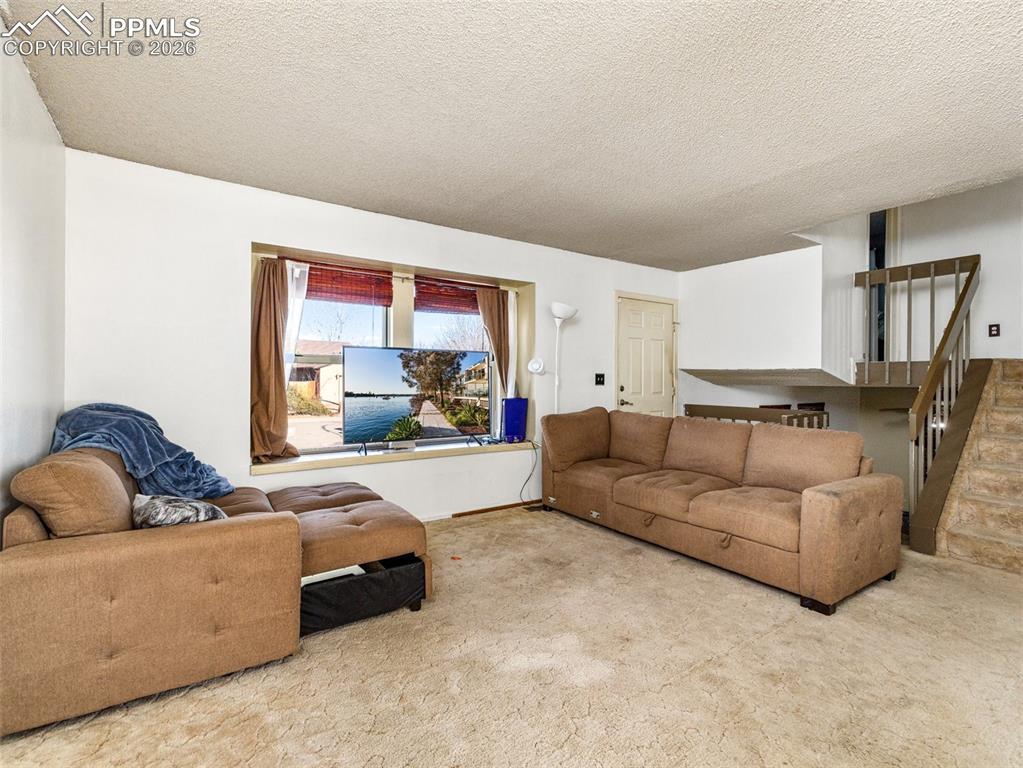 Image 5 of 30: Living room featuring a textured ceiling, carpet flooring, and stairs