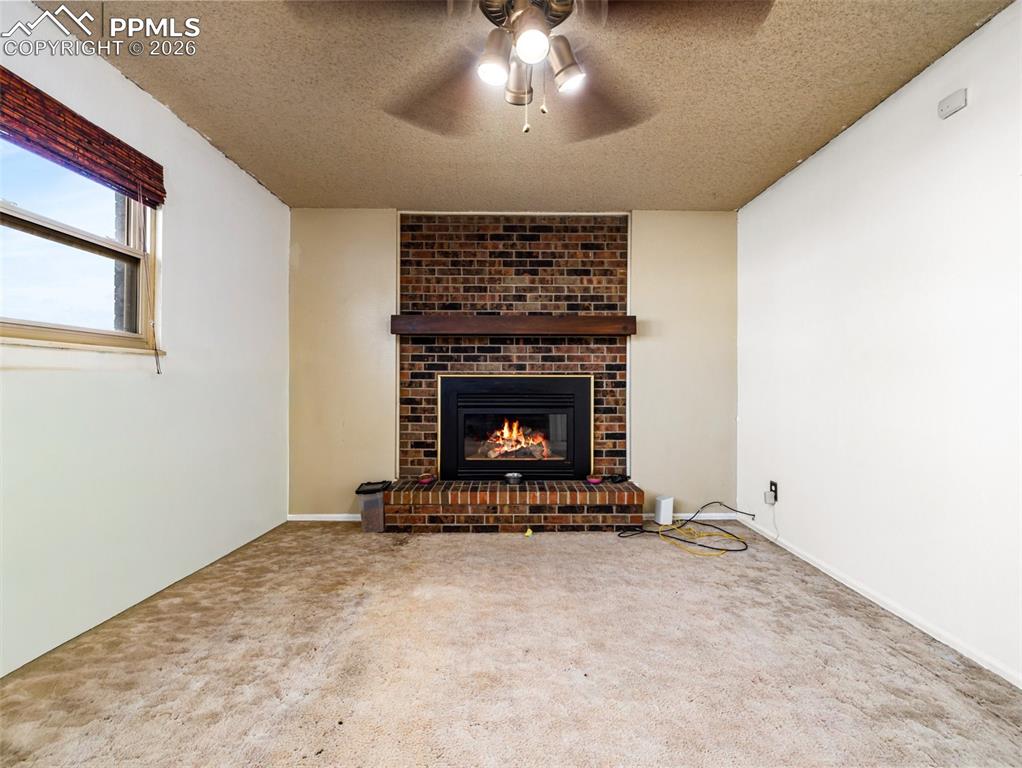 Image 9 of 30: Unfurnished living room with a fireplace, a textured ceiling, carpet, and a