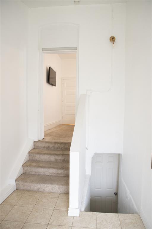 Image 13 of 15: Hallway with neutral tiled flooring and white walls, featuring carpeted sta