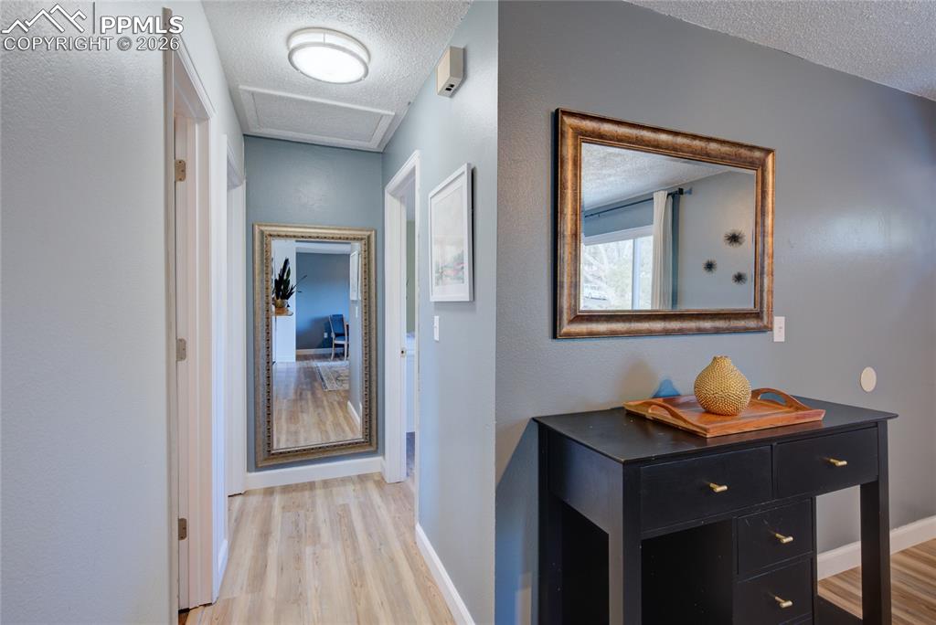 Image 12 of 35: Hall with a textured ceiling, light wood-style floors, and a textured wall