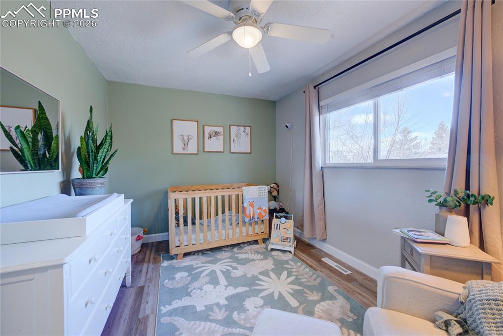 Image 16 of 35: Bedroom with a crib, dark wood-style floors, and ceiling fan