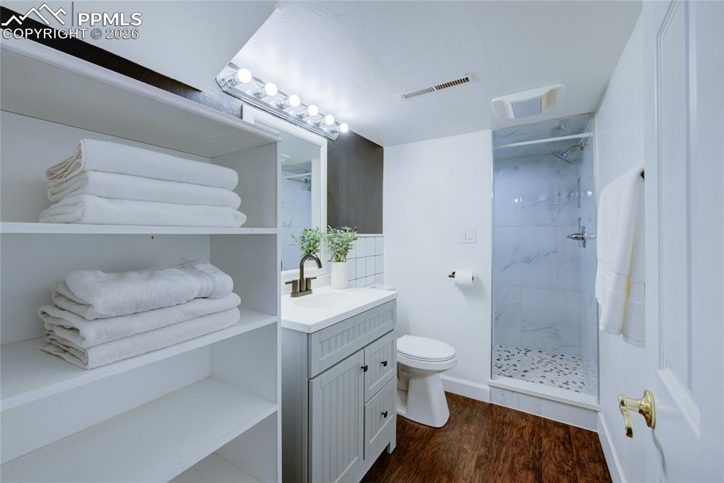 Image 25 of 35: Bathroom with vanity, a marble finish shower, and dark wood-style floors