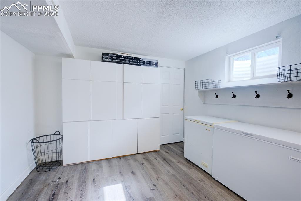Image 28 of 35: Laundry room with light wood-style flooring and a textured ceiling
