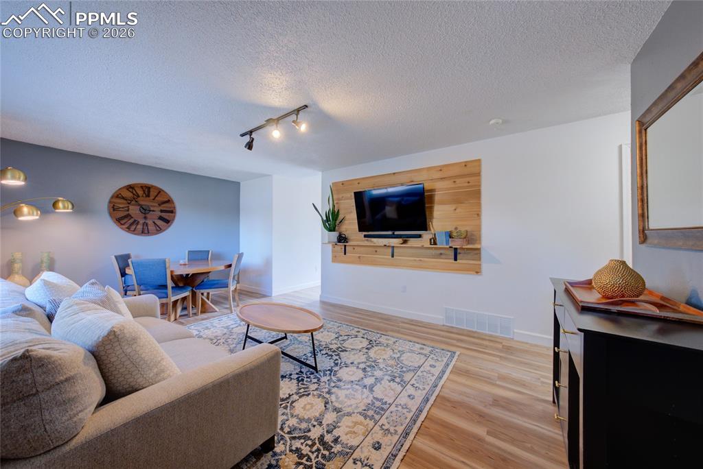 Image 5 of 35: Living room with light wood-type flooring, a textured ceiling, and rail lig