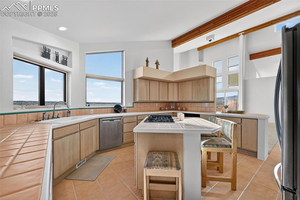 Image 16 of 50: Kitchen with tile counters, light brown cabinetry, appliances with stainles