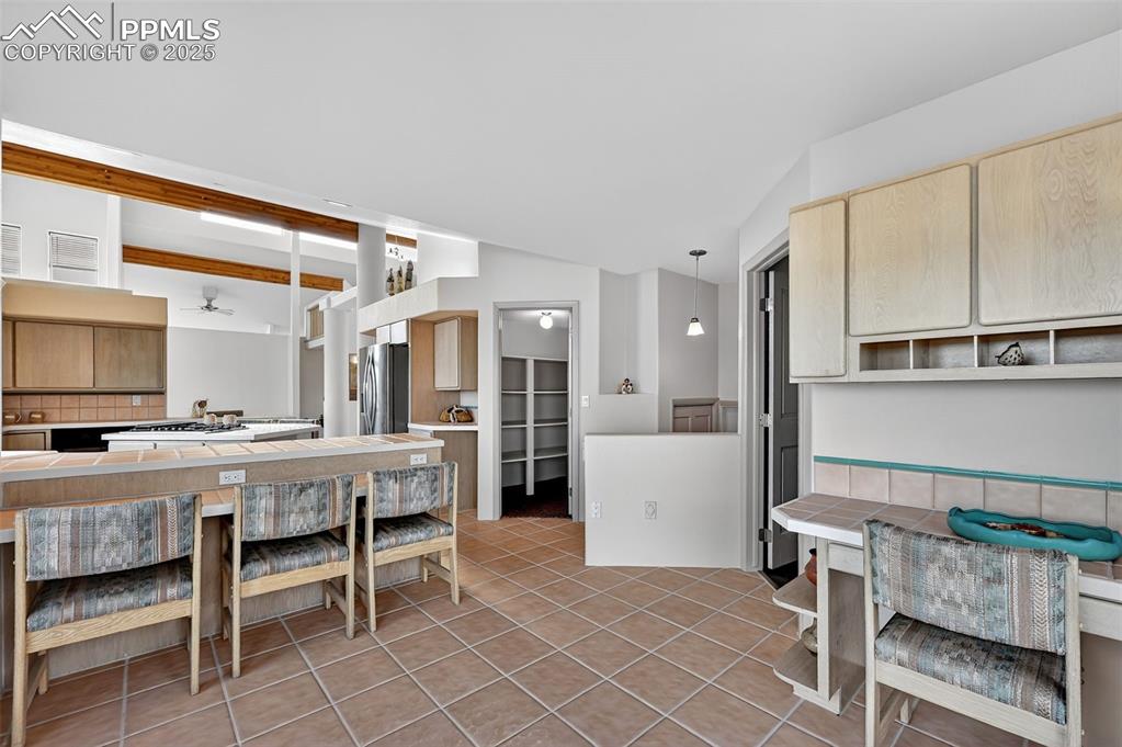 Image 18 of 50: Kitchen featuring light brown cabinets, lofted ceiling, light tile patterne