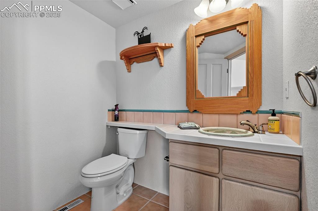 Image 22 of 50: main level 1/2 Bathroom with a textured wall, vanity, and light tile patter