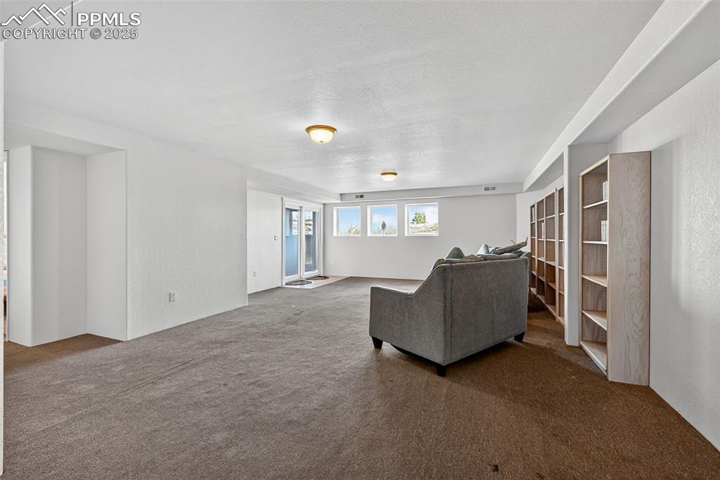 Image 34 of 50: Living area with dark colored carpet, a textured ceiling, and a textured wa
