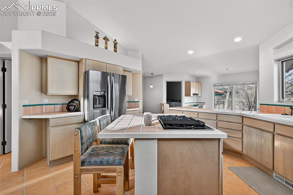 Image 8 of 50: Kitchen featuring tile counters, a center island, light brown cabinetry, st