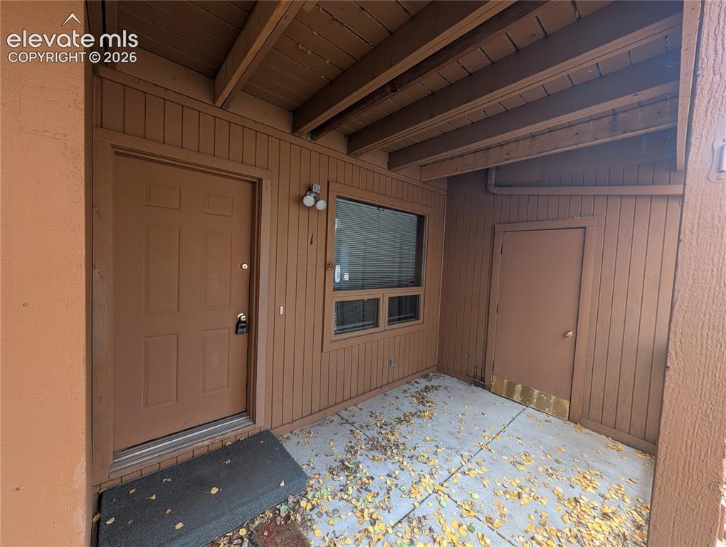 Caption: Covered entryway with concrete flooring, wood paneling, exposed ceiling beams, and exterior lighting