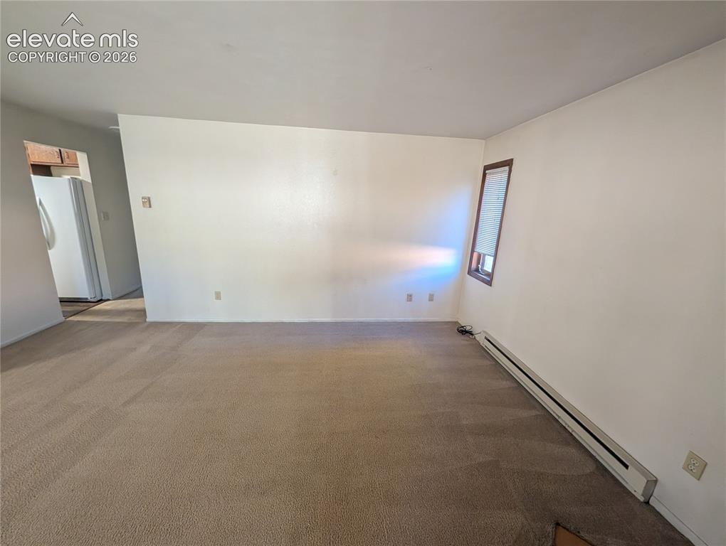 Image 10 of 30: Carpeted living area with white walls and a window with wood trim