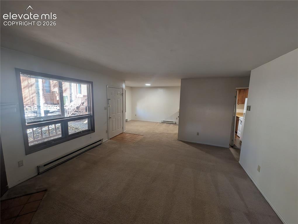 Image 7 of 30: Carpeted living space with a front entry door, a large window, and baseboar