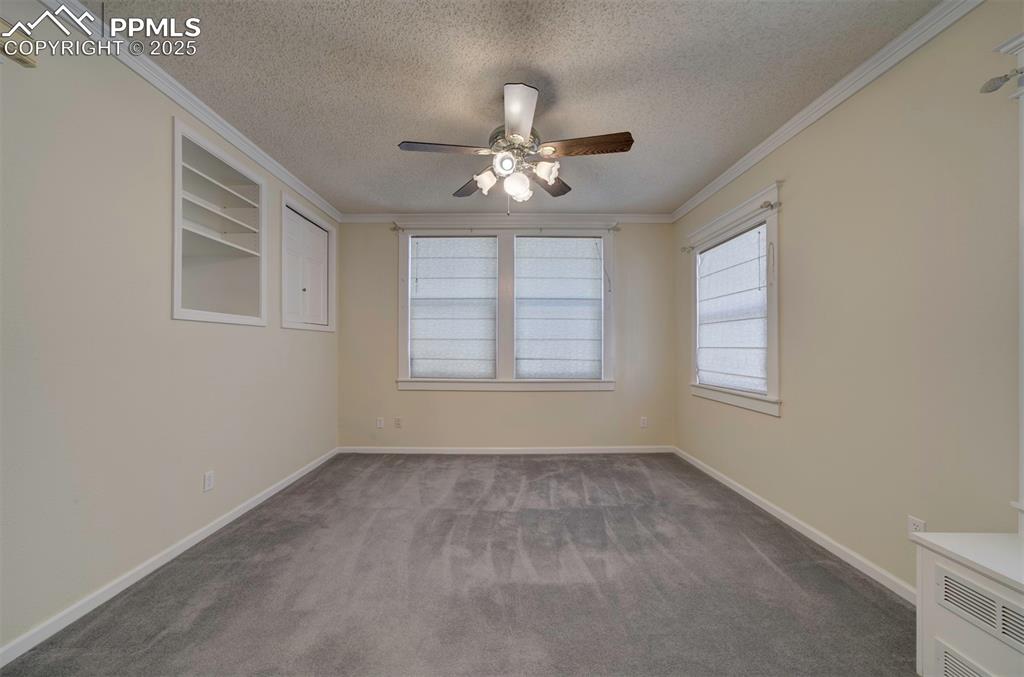 Image 26 of 40: Spare room featuring dark colored carpet, ornamental molding, a textured ce