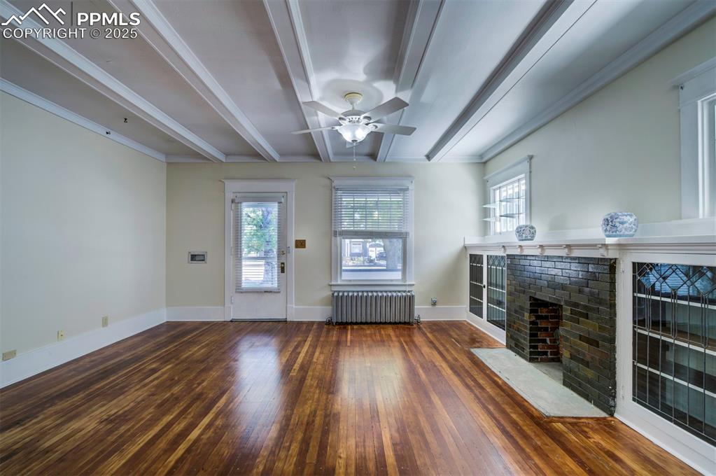 Image 8 of 40: Unfurnished living room with beamed ceiling, dark wood finished floors, ple