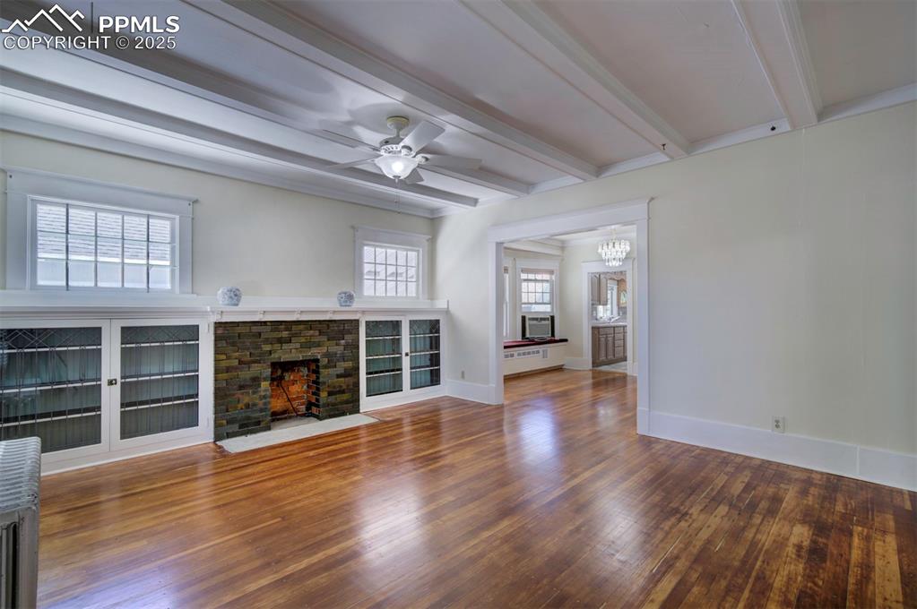 Image 9 of 40: Unfurnished living room with beamed ceiling, dark wood-style flooring, a fi