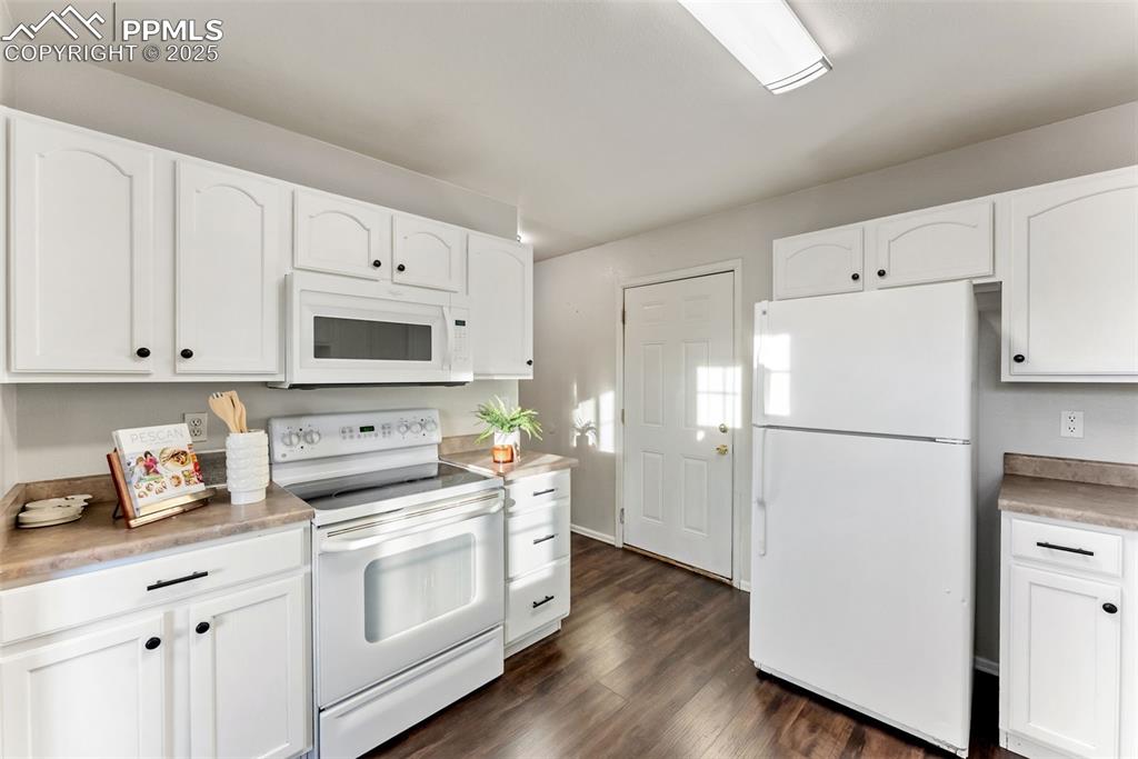 Image 11 of 45: Kitchen featuring white appliances, white cabinets, dark wood-style floorin