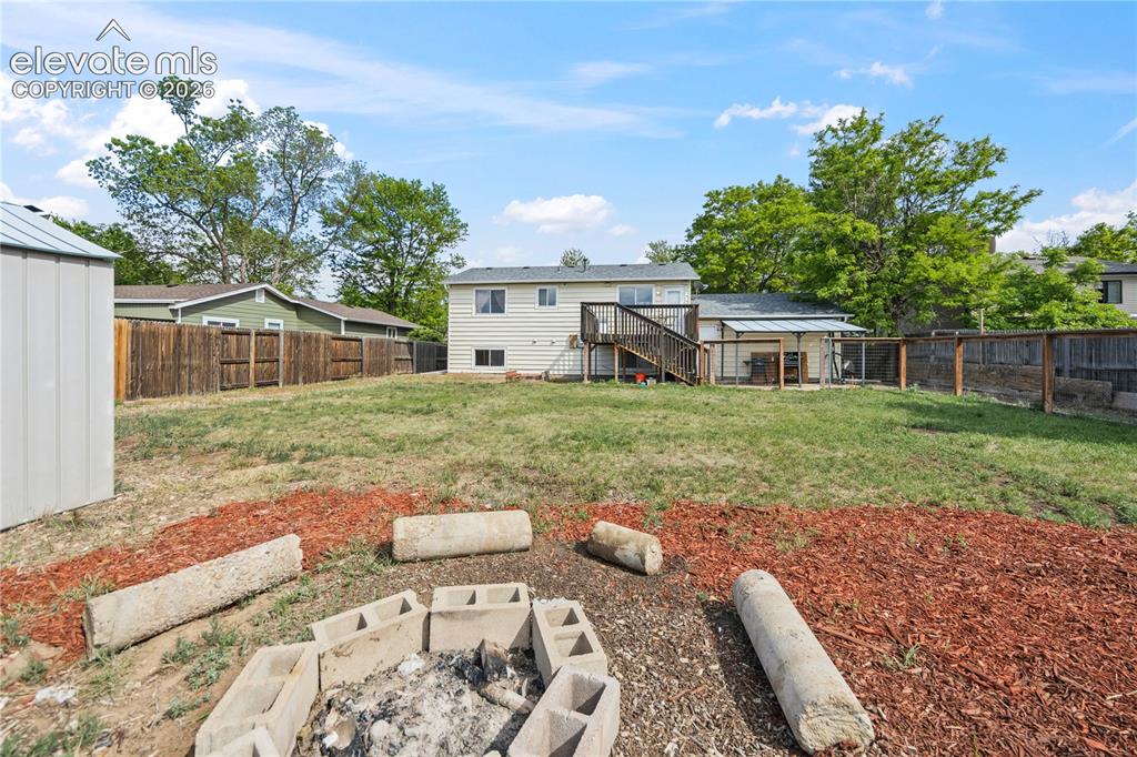 Image 28 of 31: Fenced backyard with deck, covered patio, dog run, and storage shed.