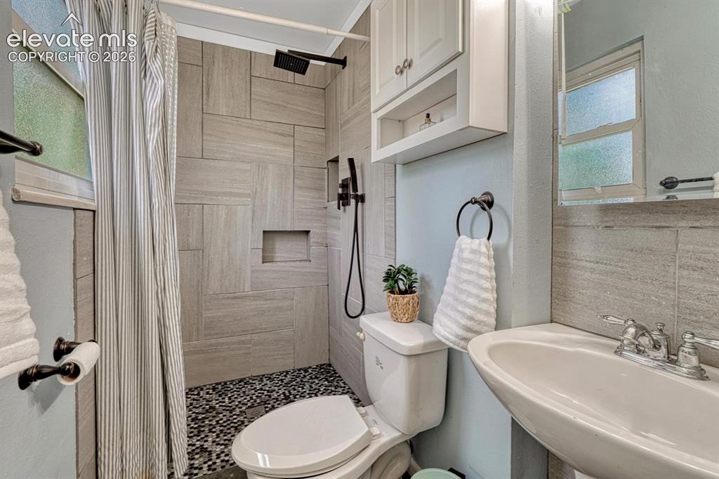 Image 32 of 50: The Primary Bathroom features a pedestal sink, mirror, cabinet, and tiled s