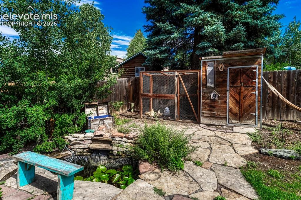 Image 40 of 50: Serene water feature surrounded by a flagstone patio, and a chicken coop to