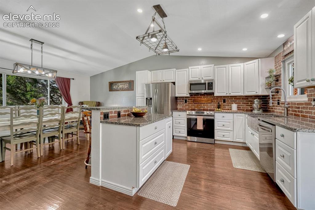 Image 9 of 50: The updated Kitchen features white cabinetry, granite countertops, a brick 