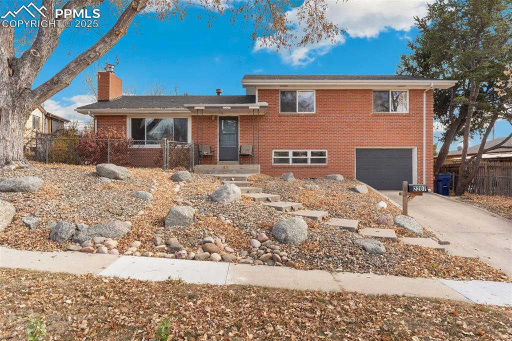 Caption: Split level home featuring concrete driveway, brick siding, a chimney, and a garage
