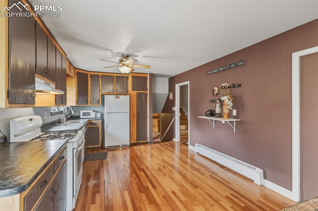 Image 15 of 37: Kitchen featuring white appliances, a baseboard radiator, light wood-style