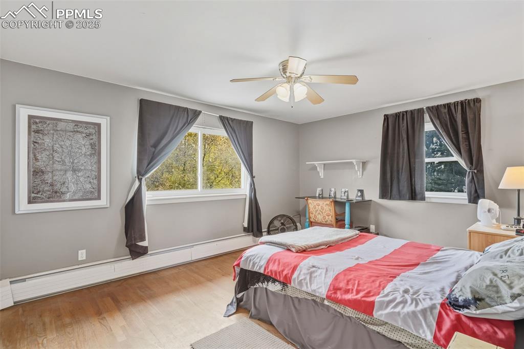 Image 16 of 37: Bedroom with baseboard heating, wood finished floors, and a ceiling fan