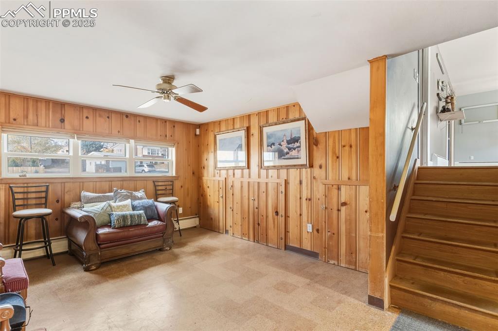 Image 24 of 37: Living area with tile patterned floors, stairway, wooden walls, baseboard h