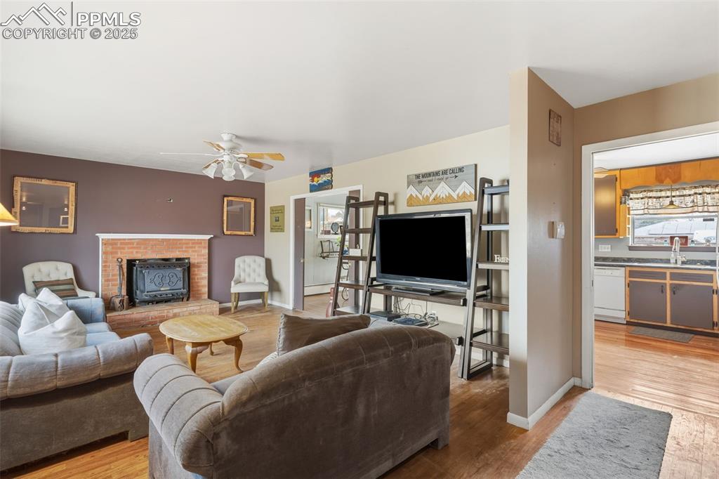 Image 8 of 37: Living area featuring light wood finished floors, a ceiling fan, and a fire