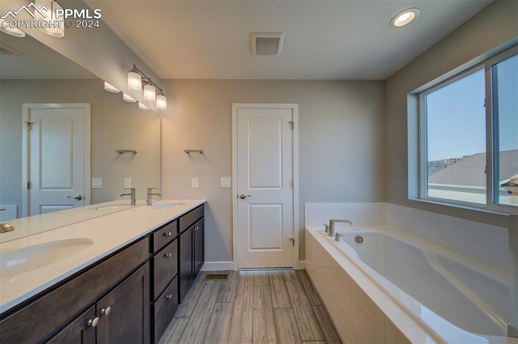 Image 39 of 47: Bathroom featuring tiled bath, hardwood / wood-style flooring, and dual bow