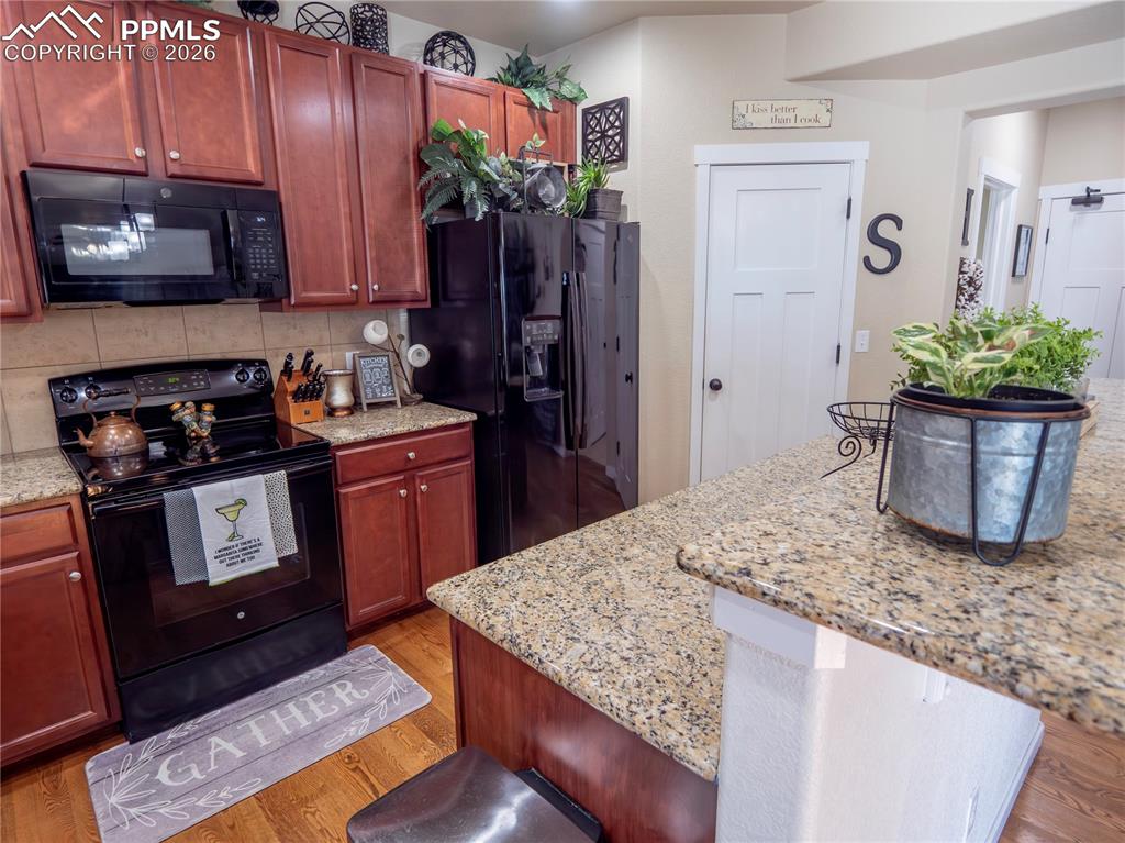 Image 12 of 32: Kitchen with black appliances, light stone counters, light wood finished fl