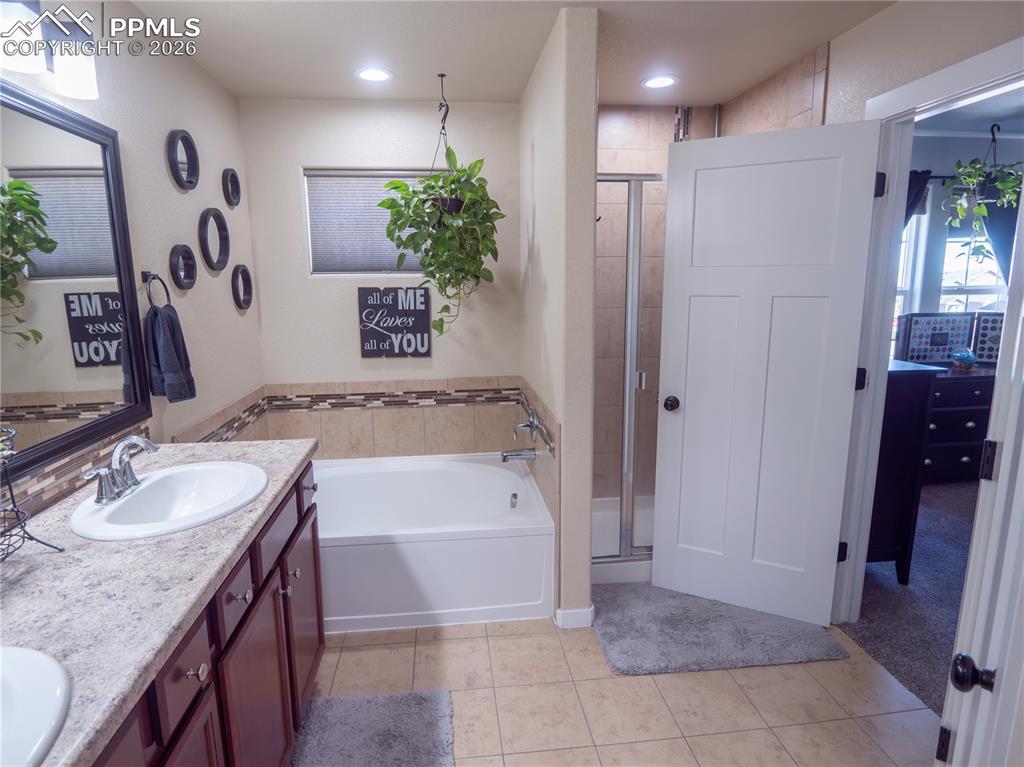 Image 25 of 32: Bathroom featuring double vanity, a shower stall, a bath, and light tile pa