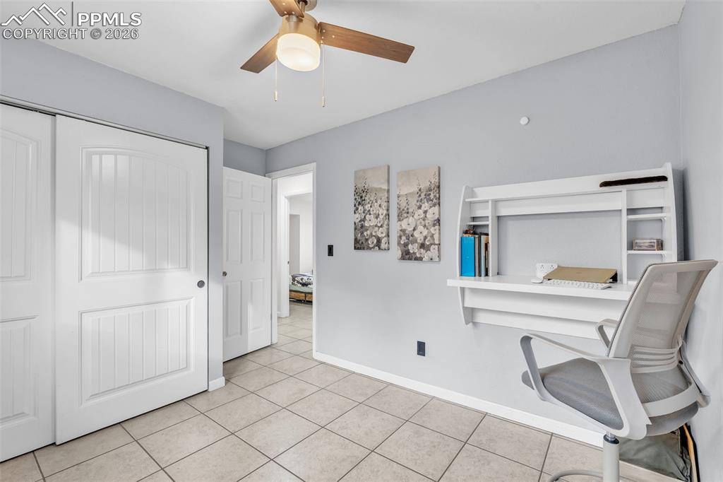 Image 32 of 44: Home office with light tile patterned floors and ceiling fan