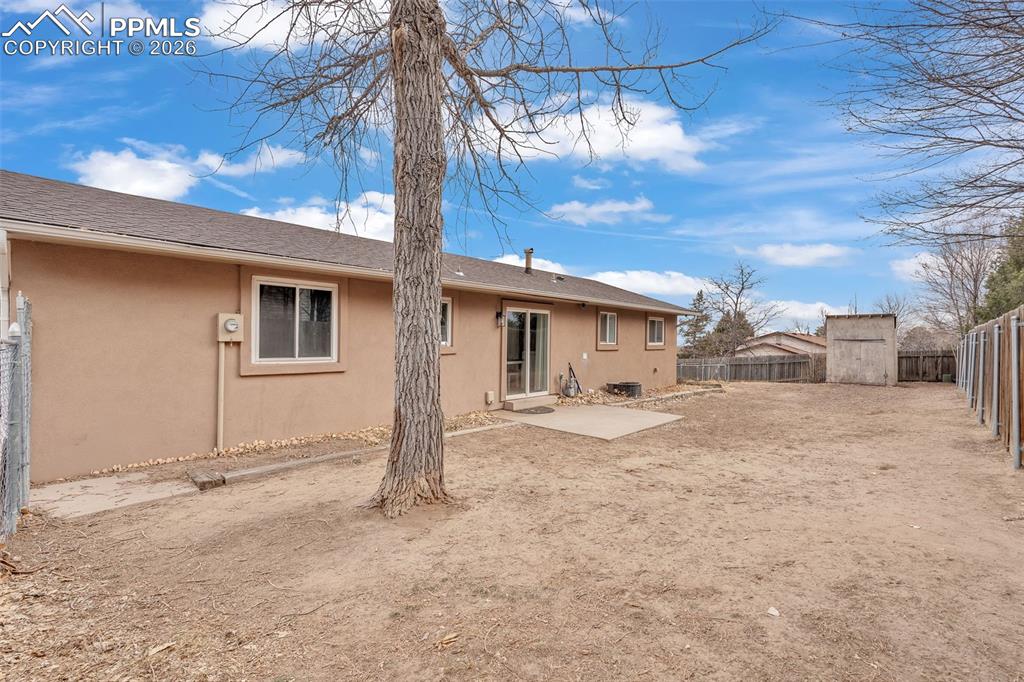 Image 35 of 44: Rear view of house featuring stucco siding, a fenced backyard, a storage sh