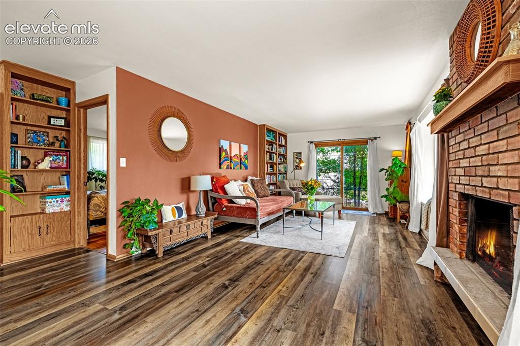 Image 11 of 38: Spacious living area featuring wood-finish flooring, a brick fireplace with