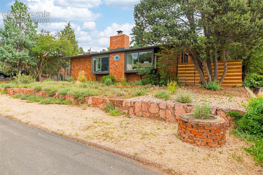 Image 2 of 38: Mid-century style residence featuring a brick facade, chimney, and large wi