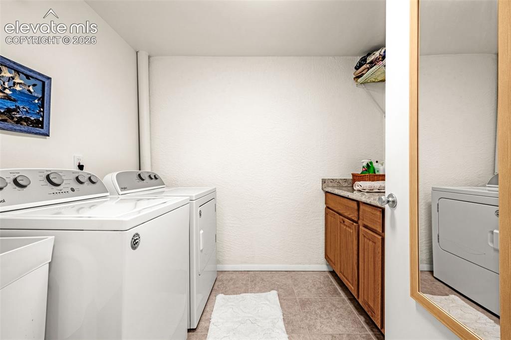 Image 30 of 38: Dedicated laundry area featuring a washer and dryer, tile flooring, wood-fi