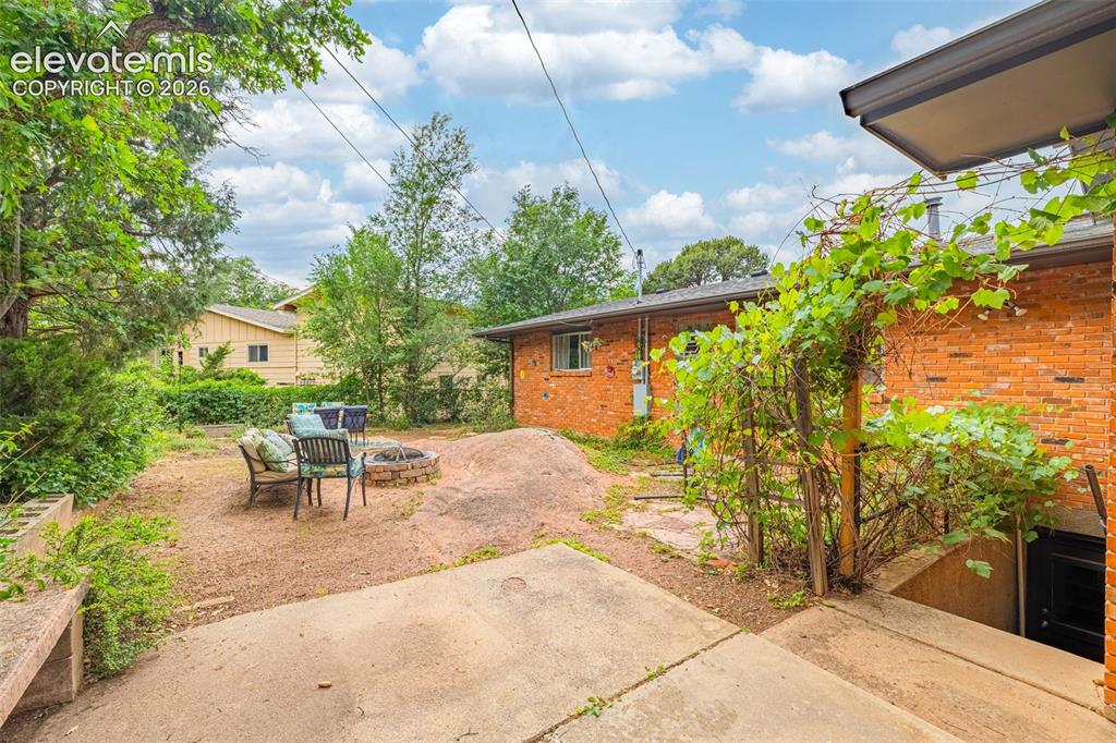 Image 35 of 38: Rear exterior featuring a brick facade, concrete patio, an arbor with climb