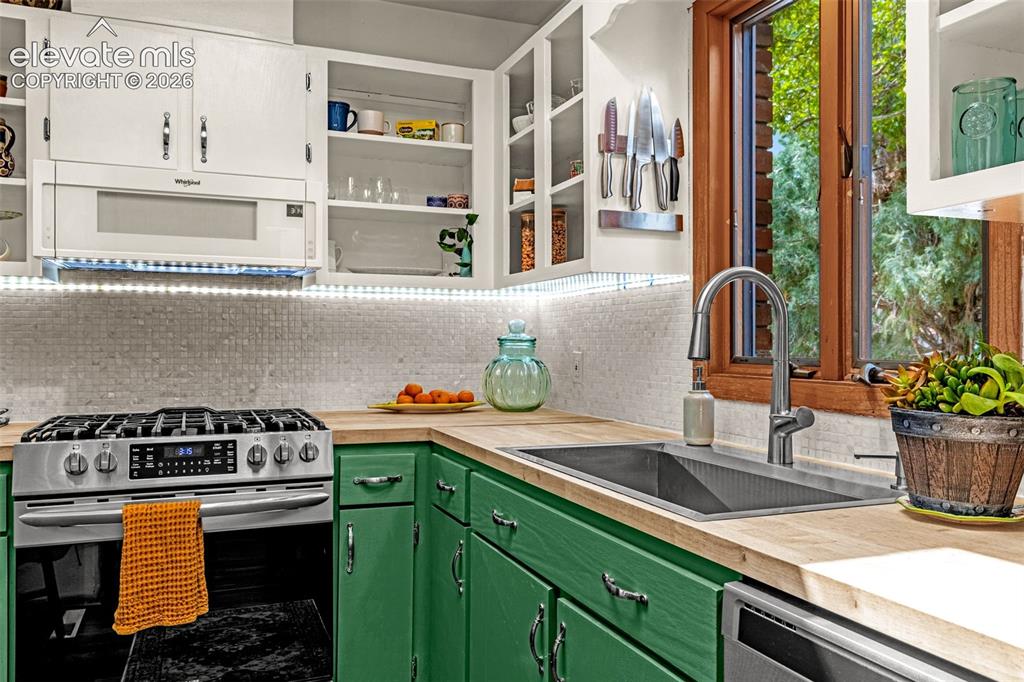 Image 7 of 38: Kitchen featuring green base cabinetry, wood-finish countertops, and a whit