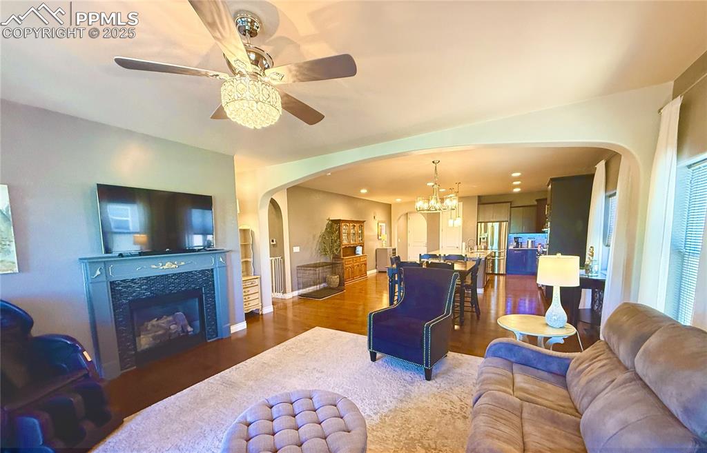 Image 10 of 40: Living room with arched walkways, wood finished floors, ceiling fan, a tile