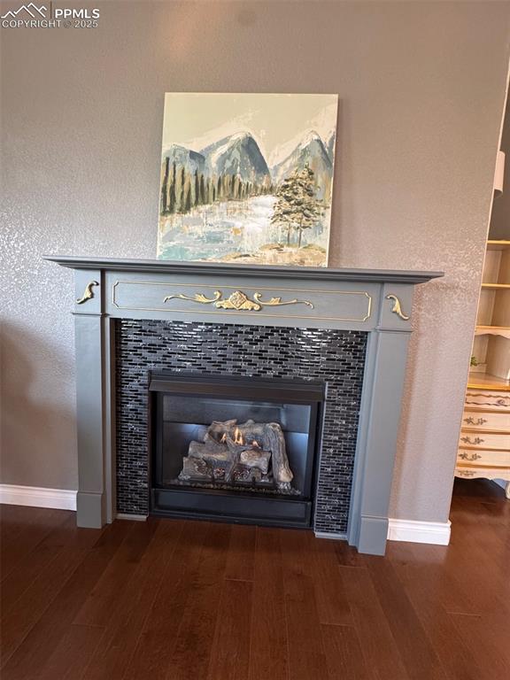 Image 11 of 40: Detailed view of a tile fireplace, wood finished floors, and a textured wal