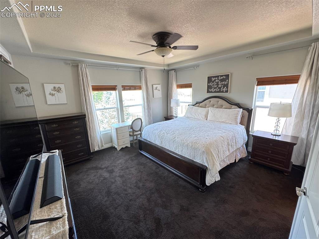 Image 12 of 40: Bedroom featuring a textured ceiling, dark colored carpet, and a ceiling fa