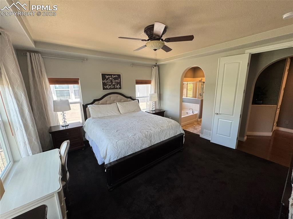 Image 13 of 40: Bedroom featuring arched walkways, a textured ceiling, multiple windows, da