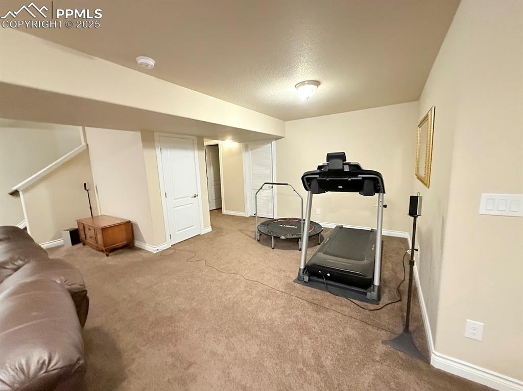 Image 19 of 40: Workout area in basement featuring a textured ceiling, baseboards, and carp