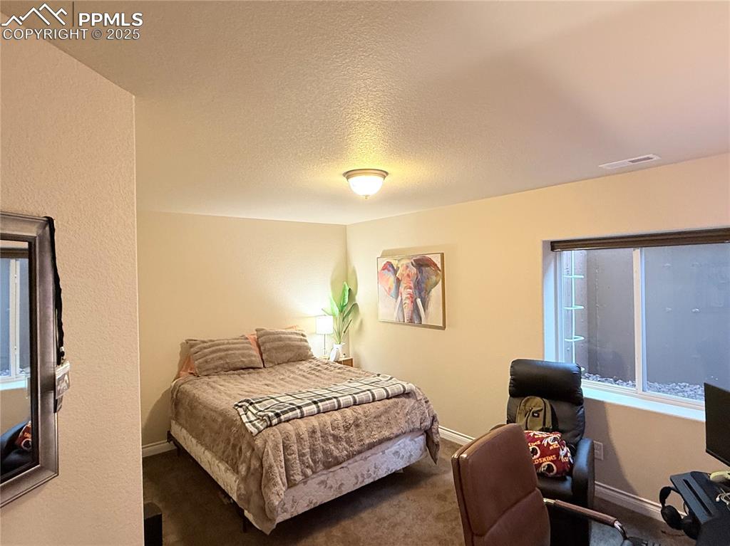 Image 21 of 40: Carpeted bedroom in basement with a textured ceiling, baseboards, and visib