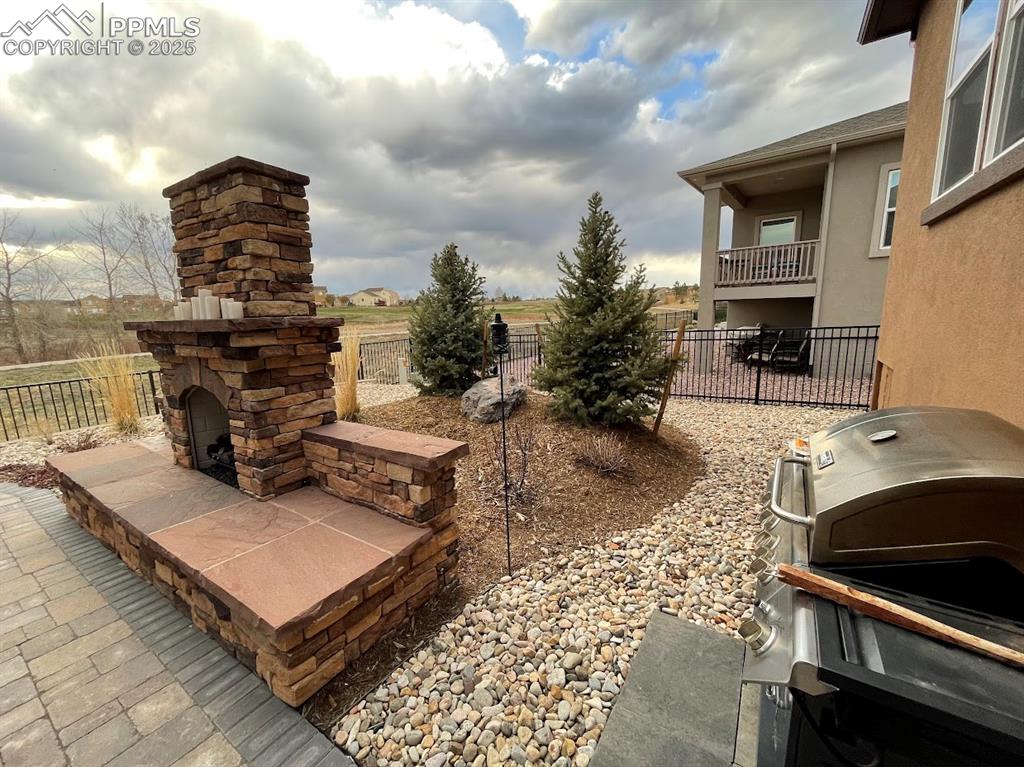 Image 34 of 40: View of patio with a fence, and an outdoor stone fireplace