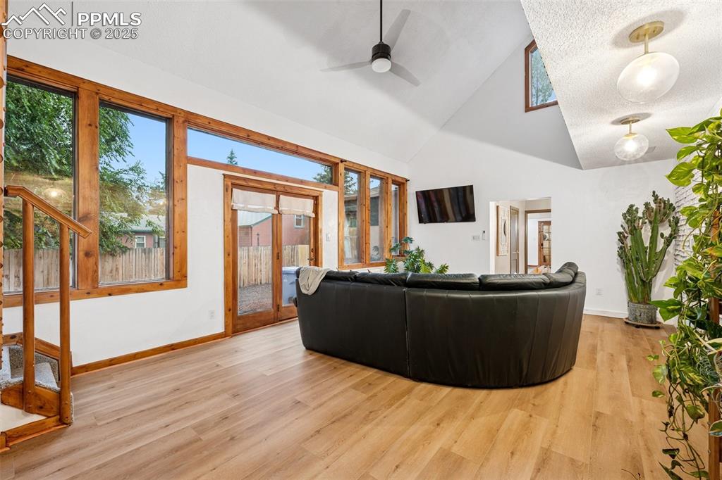 Image 19 of 48: Living area with light wood-type flooring, high vaulted ceiling, ceiling fa